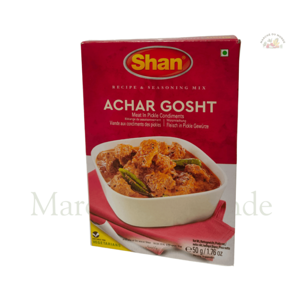 Paquet de Achar Gosht 50g à côté d’un curry de viande épicé avec une touche de pickle, garni de piments verts.